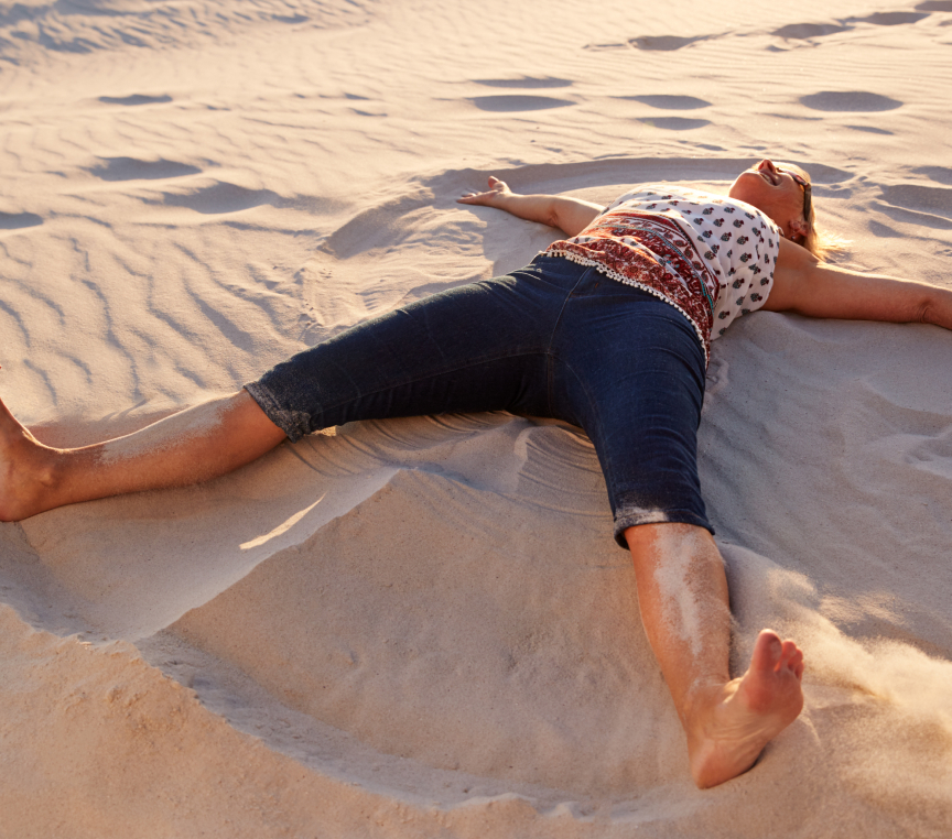 Young woman laying on the beach and playing with the sand